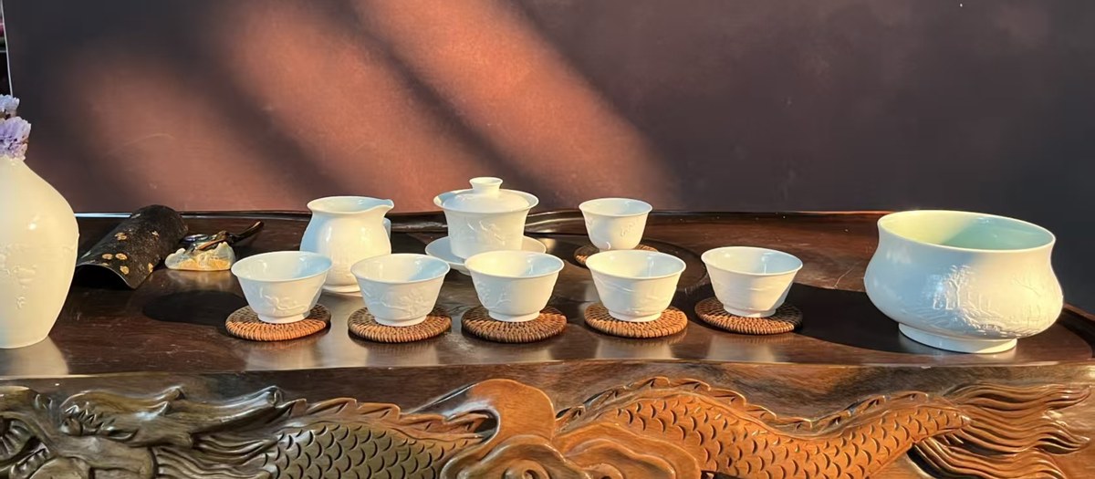 茶席布置实景：德化白瓷茶具陈于雕刻木桌，盖碗公道杯品杯依次排开